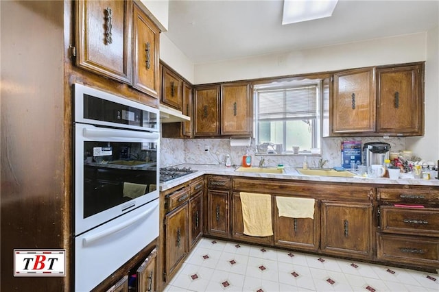 kitchen with sink, oven, decorative backsplash, stainless steel gas cooktop, and dark brown cabinetry