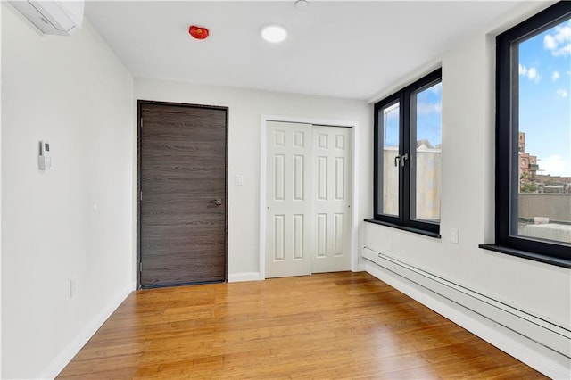 unfurnished bedroom featuring light wood finished floors, baseboard heating, and baseboards