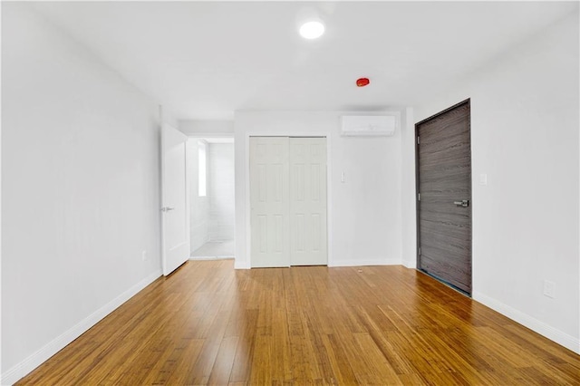 unfurnished bedroom with an AC wall unit, a closet, wood-type flooring, and baseboards