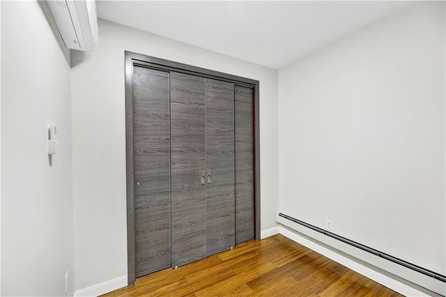 unfurnished bedroom featuring a baseboard heating unit, wood finished floors, and baseboards