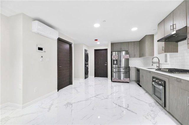 kitchen featuring stainless steel appliances, gray cabinets, a sink, stacked washing maching and dryer, and under cabinet range hood