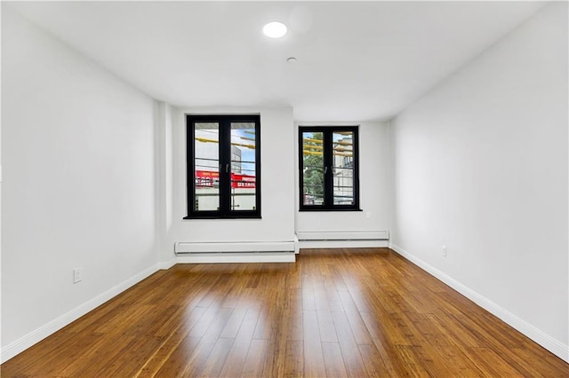 spare room featuring baseboard heating, wood-type flooring, and baseboards