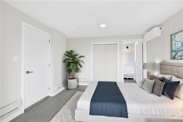 bedroom featuring a wall unit AC, baseboards, wood tiled floor, a baseboard radiator, and ensuite bath