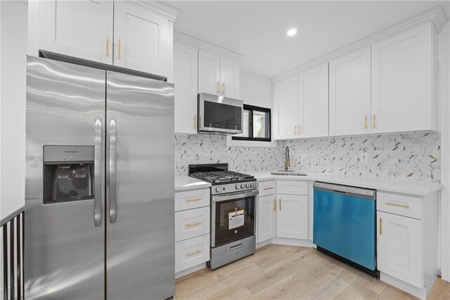 kitchen featuring sink, appliances with stainless steel finishes, white cabinetry, backsplash, and light hardwood / wood-style floors