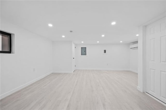 finished basement featuring light wood-type flooring, recessed lighting, electric panel, and a wall mounted air conditioner