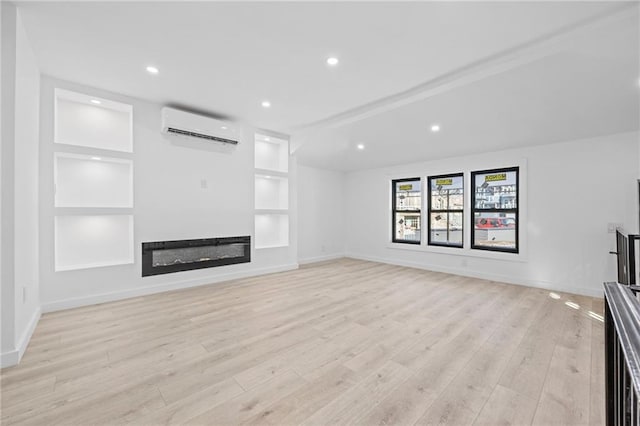 unfurnished living room featuring built in features, a glass covered fireplace, light wood-type flooring, a wall mounted air conditioner, and baseboards