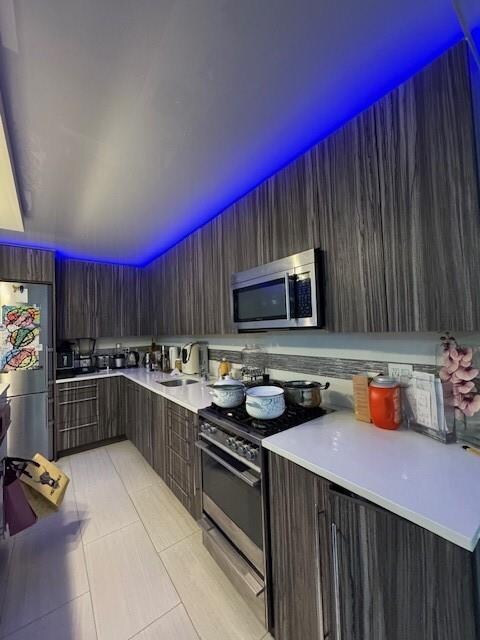 kitchen with stainless steel appliances, light tile patterned flooring, dark brown cabinets, and sink