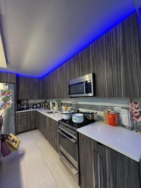 kitchen featuring appliances with stainless steel finishes, sink, light tile patterned floors, and dark brown cabinets