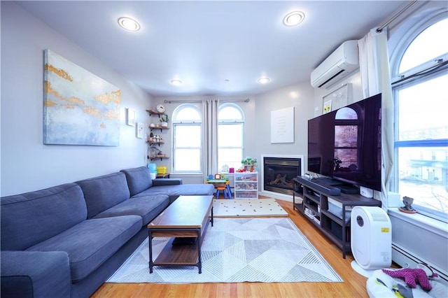 living room with a glass covered fireplace, light wood-style flooring, baseboard heating, an AC wall unit, and recessed lighting