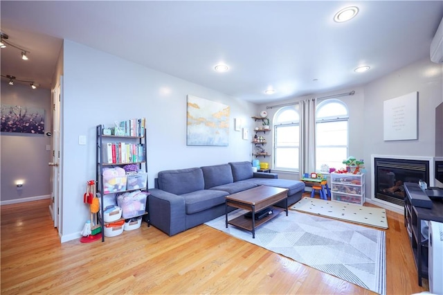 living room with rail lighting, baseboards, wood finished floors, and a glass covered fireplace