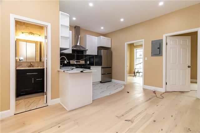 kitchen featuring electric panel, light wood-type flooring, backsplash, and wall chimney exhaust hood