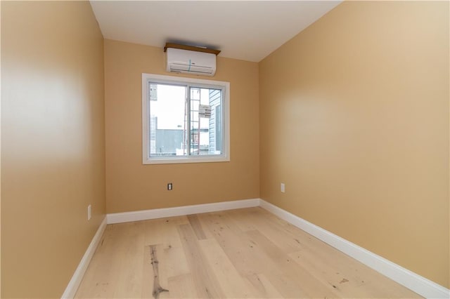 spare room featuring light wood-style floors, a wall mounted AC, and baseboards