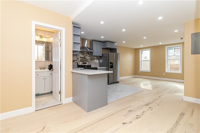 kitchen featuring a peninsula, decorative backsplash, light countertops, appliances with stainless steel finishes, and wall chimney range hood