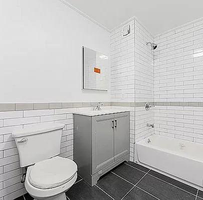 full bathroom featuring tile patterned flooring, tile walls, tiled shower / bath combo, vanity, and toilet