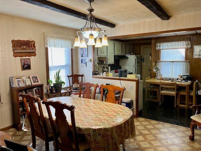 dining area featuring an inviting chandelier, beamed ceiling, and wood walls