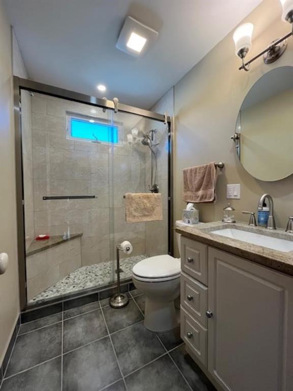 bathroom featuring vanity, toilet, an enclosed shower, and tile patterned flooring