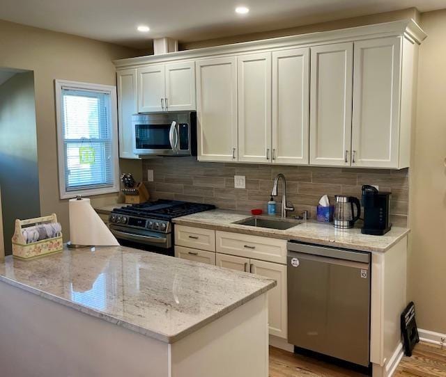 kitchen with stainless steel appliances, sink, white cabinets, and light stone counters