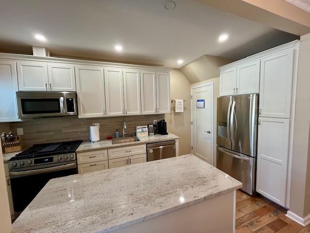 kitchen with white cabinetry, stainless steel appliances, sink, and light stone counters