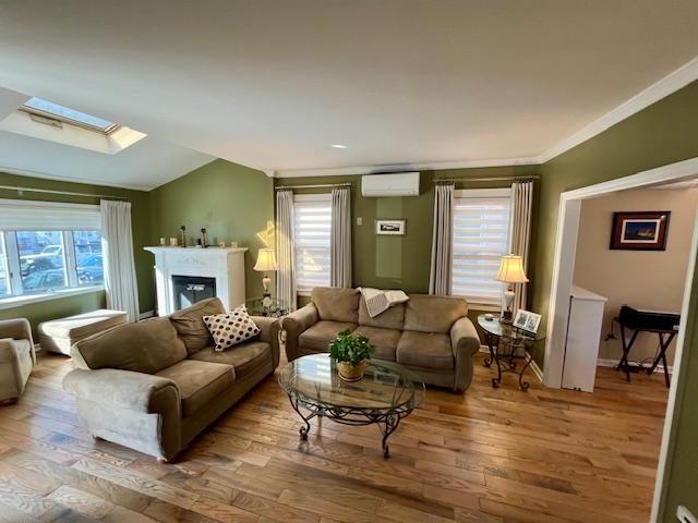 living room with crown molding, hardwood / wood-style flooring, vaulted ceiling with skylight, and a wall mounted AC