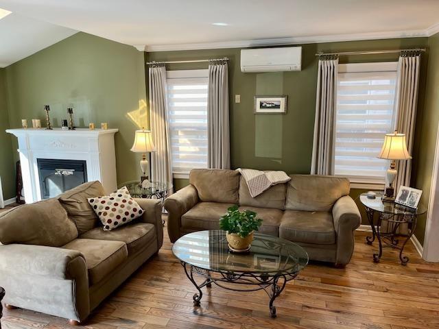 living room with lofted ceiling, wood-type flooring, and a wall mounted AC