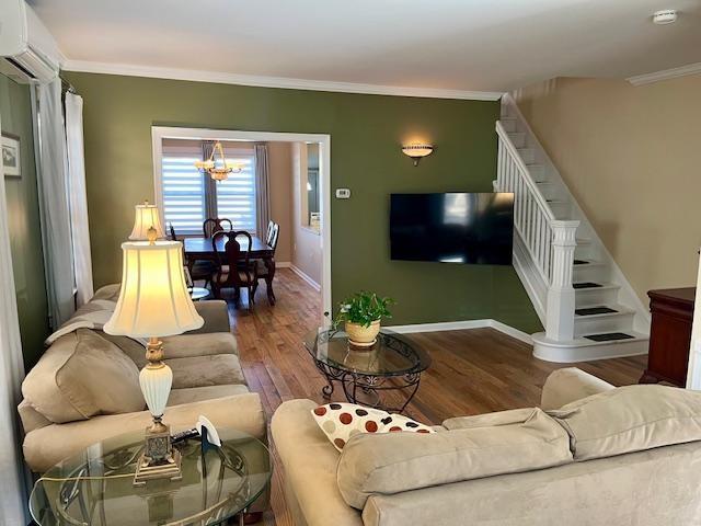 living room with ornamental molding, a chandelier, hardwood / wood-style floors, and an AC wall unit