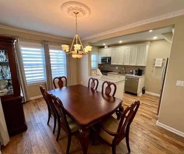 dining space featuring an inviting chandelier, sink, crown molding, and light hardwood / wood-style floors