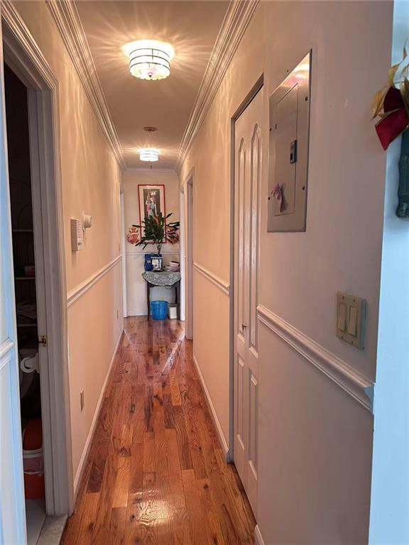 hallway with ornamental molding, electric panel, and wood-type flooring