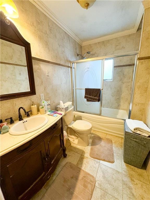 full bathroom with tile walls, bath / shower combo with glass door, vanity, ornamental molding, and toilet