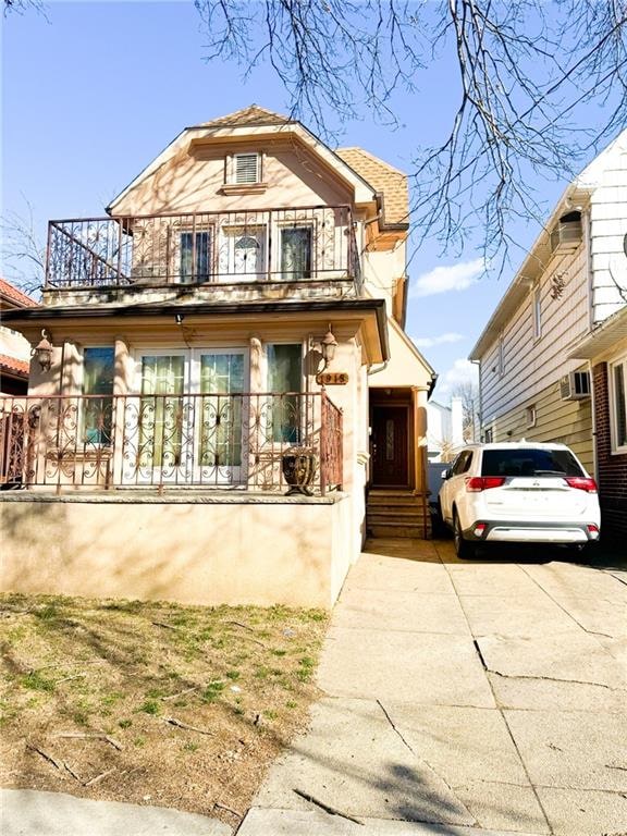 view of front facade featuring a wall mounted air conditioner, concrete driveway, and a balcony