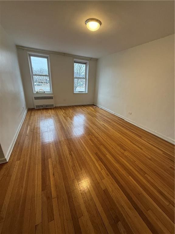 spare room featuring baseboards, wood-type flooring, and radiator heating unit