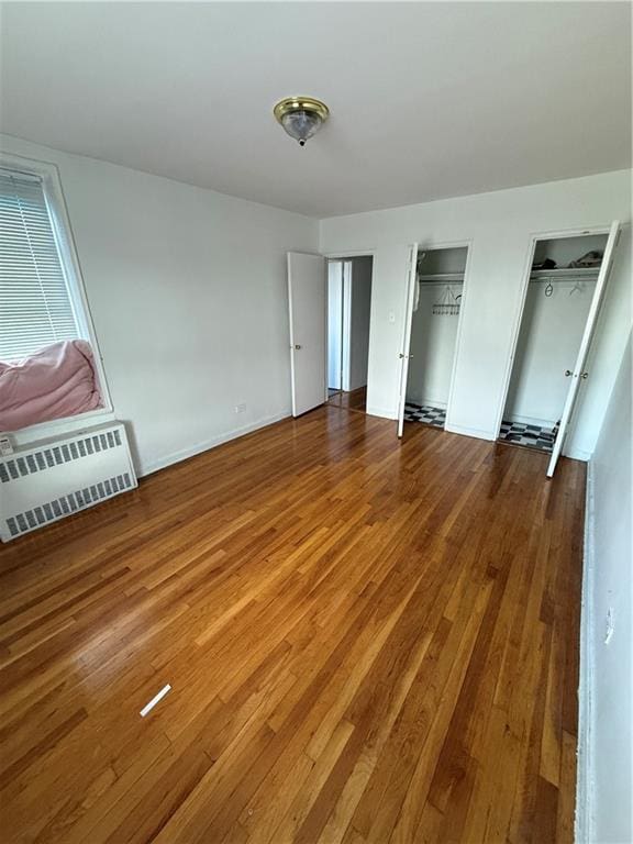 unfurnished bedroom with multiple closets, radiator heating unit, and wood-type flooring