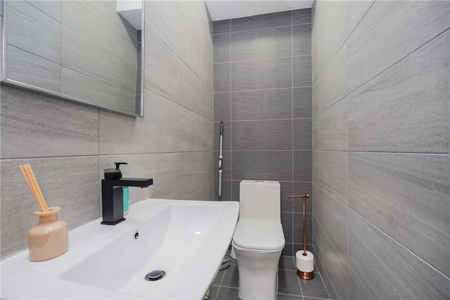 half bathroom featuring toilet, tile patterned flooring, tile walls, and a sink