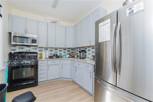 kitchen with stainless steel appliances, light stone counters, backsplash, and light wood-style flooring