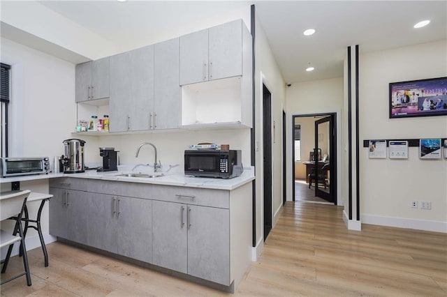 kitchen featuring black microwave, gray cabinetry, a sink, light wood-type flooring, and open shelves