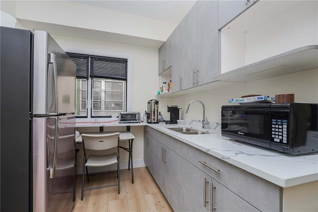 kitchen with light stone counters, freestanding refrigerator, gray cabinets, black microwave, and a sink