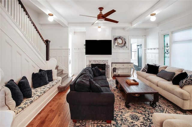 living room with hardwood / wood-style flooring, a tile fireplace, ceiling fan, and beam ceiling