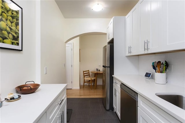 kitchen with arched walkways, white cabinetry, light countertops, dishwasher, and tasteful backsplash