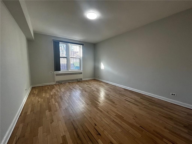 empty room featuring baseboards, dark wood-type flooring, and radiator