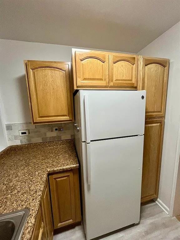 kitchen featuring tasteful backsplash, brown cabinetry, a sink, and freestanding refrigerator