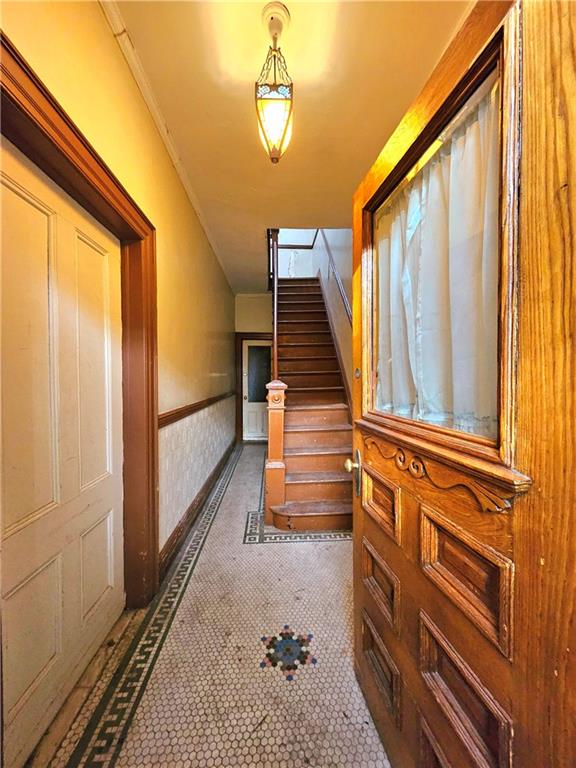 hall with ornamental molding, tile patterned flooring, wainscoting, and stairway