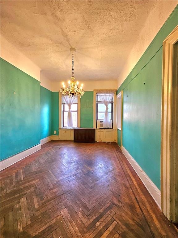 spare room with an inviting chandelier, dark parquet floors, and a textured ceiling