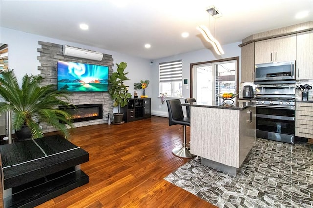 kitchen featuring a stone fireplace, a breakfast bar area, an AC wall unit, dark hardwood / wood-style flooring, and stainless steel appliances