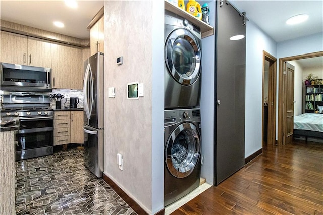 clothes washing area with stacked washer and dryer, baseboards, laundry area, and dark wood-style flooring