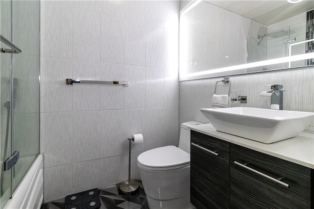 full bath featuring toilet, shower / bath combination with glass door, vanity, and tile walls