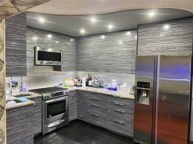 kitchen with dark tile patterned floors, light stone countertops, appliances with stainless steel finishes, and tile walls