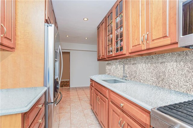 kitchen featuring light tile patterned flooring, tasteful backsplash, sink, stainless steel fridge, and light stone counters