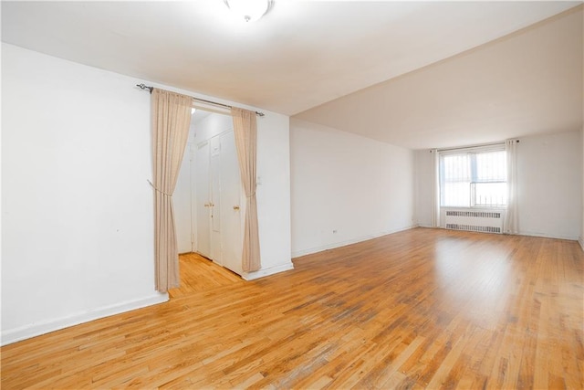 empty room with radiator, baseboards, and light wood-style floors