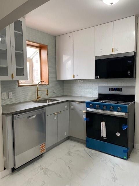 kitchen with marble finish floor, gray cabinetry, appliances with stainless steel finishes, glass insert cabinets, and a sink