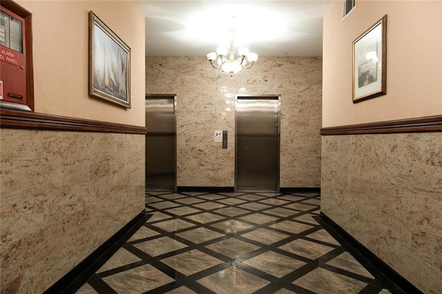 interior space with a chandelier, a wainscoted wall, visible vents, baseboards, and elevator