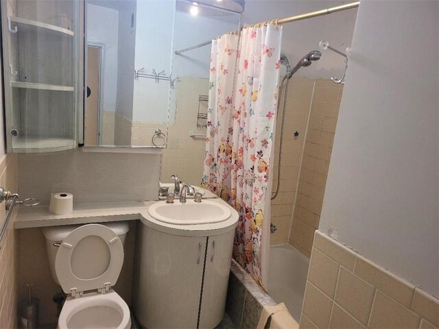 full bathroom with shower / bathtub combination with curtain, vanity, tile walls, and toilet